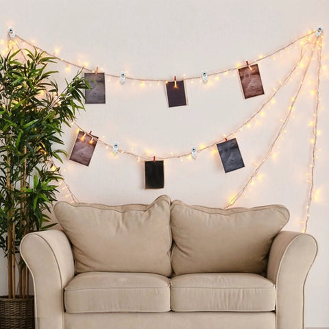 Cozy living room setup with string lights and photos hanging on wires above a beige loveseat and a green houseplant.