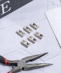Close-up of 6 roll-in T-nuts with ball spring for 10 series aluminum extrusion profiles, 1/4-20 size, zinc plated steel on table with pliers