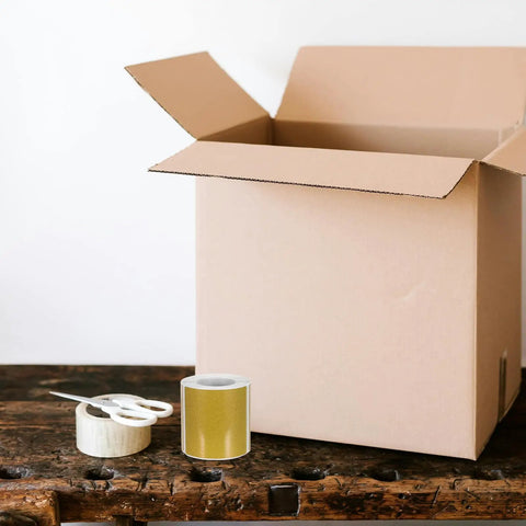 Golden Thermal Label Paper For Shipping And Mailing Self Adhesive Labels With Smooth Surface next to open cardboard box on table