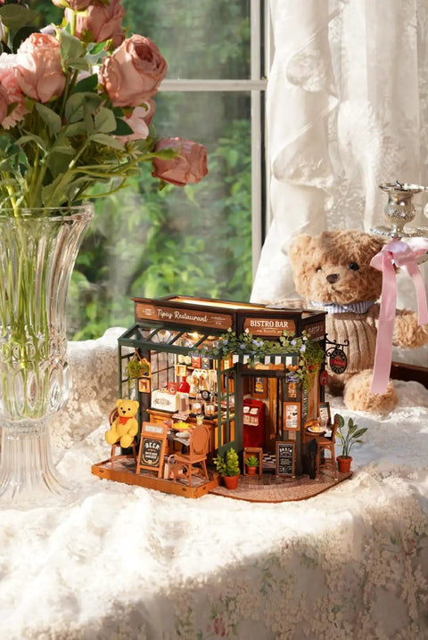 Charming Bistro Style Miniature House Kit With LED For Adults Beginners DIY Wooden Dollhouse Cozy Cafe Vibe Perfect Mother's Day Or Birthday Gift 9.37 By 7.09 By 7.17 Inches on table with teddy bear and flowers