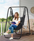 Outdoor setting with grey heavy duty rustproof hammock chair with stand and ergonomic U bracket, woman reading on porch