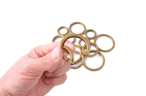 Hand holding 4 Pack Round Carabiner Key Rings With Spring Snap Clips And Flat O Rings In Brushed Brass Finish, multiple in background.