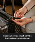 Master Lock black 3-digit combination padlock being attached to a gray hard-shell suitcase