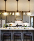 Three Black Farmhouse Pendant Light With Clear Glass Schoolhouse Style fixtures above a modern kitchen island with gray cabinetry.