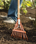 Narrow Shrub Rake For Tight Spots, 8 Inch Wide Head, in use in a garden with durable hardwood grip and reinforced tines.