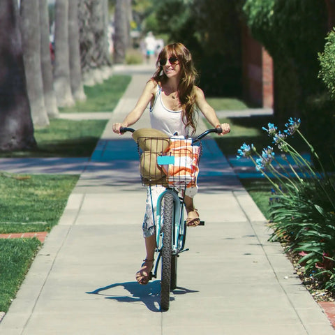 Woman riding bicycle down a path with a basket, trees lining the walkway.