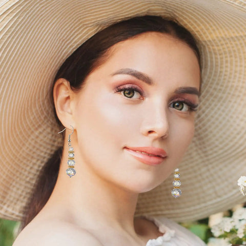 Woman wearing dangling earrings with sparkling beads, large sun hat, and floral blouse, showcasing jewelry accessories.