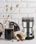 Electric Coffee And Spice Grinder Handheld 150W Quick Grinding With Stainless Steel Blades next to coffee beans and cup