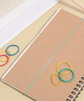 60 Pcs Rubber Pulley Belt Set For RC Cars Airplanes Robots Trucks And DIY Models Durable Transmission Belts In Multiple Sizes 23mm To 60mm Includes Colored Rubber Bands Must Have Replacement Parts And Toy Accessories placed on a notebook with colorful rubber bands.