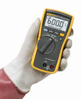 Gloved hand holding True RMS Utility Multimeter For DIY And Pros Measures AC DC Voltage, Resistance, Capacitance, Continuity And Diode Tests.