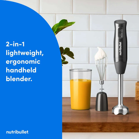 Lightweight Ergonomic Handheld Immersion Blender With Rustproof Stainless Steel Whisk Attachment And Heavy Duty Heat Resistant Shaft For Mixing Straight Out Of The Pot Dark Gray Kitchen Game Changer next to a glass of smoothie.