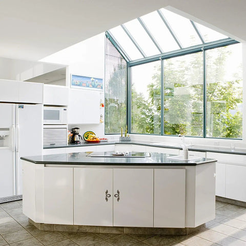 Modern kitchen with sunlight from large windows, white cabinets, sleek countertop, and integrated appliances.
