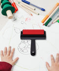 Solid Grip Rubber Paint Roller For Printmaking And Classroom Art Projects with red frame on a cluttered art table.
