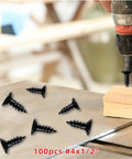 Premium Black Stainless Steel Wood Screws Featuring Flat Phillips Heads Rust Resistant Finish Smooth Driving Action Ideal For Plywood And Softwoods 100 Pack Size 4 By Half Inch laid out on wood surface with a drill.