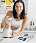 Woman using blender next to Pro Grade Digital Kitchen Scale With 66 Pound Capacity For Baking And Cooking A Large Food Scale In Stainless Steel