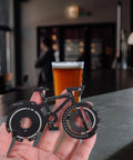 Hand holding compact bicycle shaped multitool keychain made from durable stainless steel for on the go bike repairs in a café.