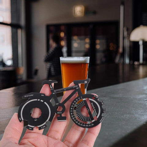 Hand holding compact bicycle shaped multitool keychain made from durable stainless steel for on the go bike repairs in a café.
