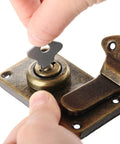 Hand inserting key into vintage metal key hasp lock for jewelry box and wooden suitcase with antique toggle latch.