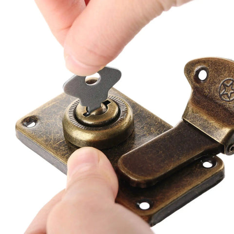 Hand inserting key into vintage metal key hasp lock for jewelry box and wooden suitcase with antique toggle latch.