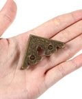 Antique Bronze Metal Corner Protectors Set Of 8 Decorative Brackets for wood furniture shown in hand for scale.