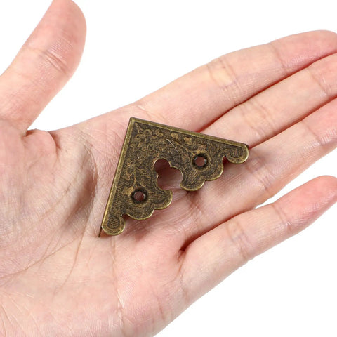 Antique Bronze Metal Corner Protectors Set Of 8 Decorative Brackets for wood furniture shown in hand for scale.