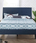 Blue upholstered bed frame with geometric patterned bedding in a modern bedroom setting.