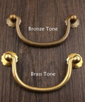Six Pack Traditional Bail Cabinet Pulls In Antique Brass For Dresser Drawers And Cabinets, top view, bronze and brass tones, wood background.