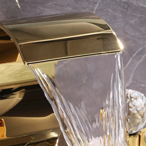 Close-up of gold bathroom sink faucet high arc waterfall spout with crystal knobs, part of 8 inch widespread solid brass design.