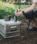 Rugged Folding Storage Box With Lid Heavy Duty Aluminum Frame Stackable Gear Crate Built Tough For Camping And Picnics No Sweat Organization Haul Your Stash On The Go Rust Resistant Silver Design with kettle and cups.