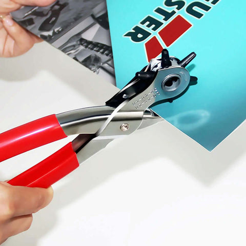 Hand using Beefy Leather Hole Puncher Workhorse With Six Punch Sizes for belts, straps, and fabric, featuring red handles.