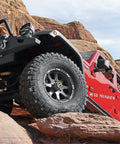 Red off-road vehicle on rocky terrain showcasing Premium Manual Locking Hub Kit With 19 Spline Fit Zinc Aluminum Dial Dual Seals Chrome Finish