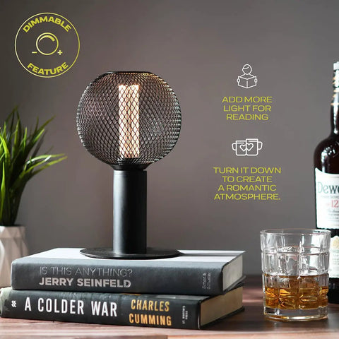 Vintage LED Edison Bulb With Black Metal Cage For Home Use Warm 2200K Soft White 3.5W Low Power Dimmable Bulb With E26 Medium Base Ideal For Table Lamps Pendants Open Socket Decor on a table lamp next to books and drinks.