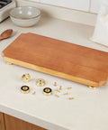 Solid Brass Cutting Board Feet With Grippy Silicone Pads on a wooden board with screws and parts on a kitchen counter.