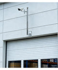 Built Tough Heavy Duty Stainless Steel Security Camera Poles And Outdoor Surveillance Posts For Bullet Dome And Wall Mounted Cams featuring rust-proof design mounted on warehouse wall.
