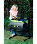 Woman using City Sleek Two Stage Compost Tumbler For Fast, Foolproof Outdoor Composting With Aeration Holes, Rust Proof Metal Plastic