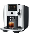 Premium Fully Automatic Chrome Espresso Coffee Machine Featuring A Hella Smooth Four Point Three Inch Smart Touchscreen Display For Twenty Seven Freshly Ground Drinks with a glass of espresso.