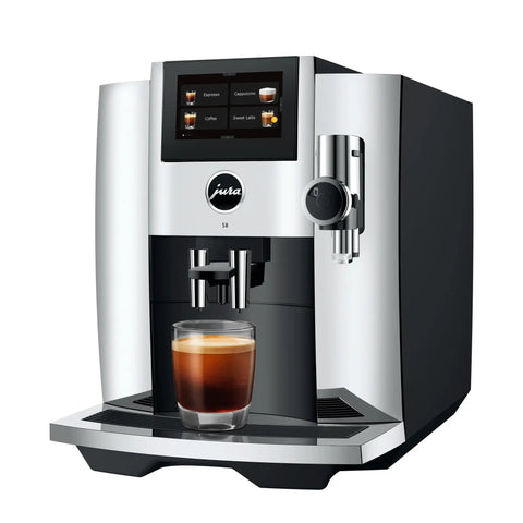 Premium Fully Automatic Chrome Espresso Coffee Machine Featuring A Hella Smooth Four Point Three Inch Smart Touchscreen Display For Twenty Seven Freshly Ground Drinks with a glass of espresso.