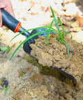 Lightweight Fireplace Shovel 12.6 Inch Ash Shovel scooping soil with a plant, carbon steel head, heat-resistant rubber handle.