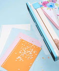 Person using adjustable 30 hole binding punch for discbound notebooks and journals on colored paper, showing punched holes and clear scale guide.