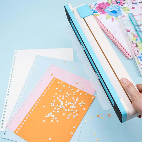 Person using adjustable 30 hole binding punch for discbound notebooks and journals on colored paper, showing punched holes and clear scale guide.