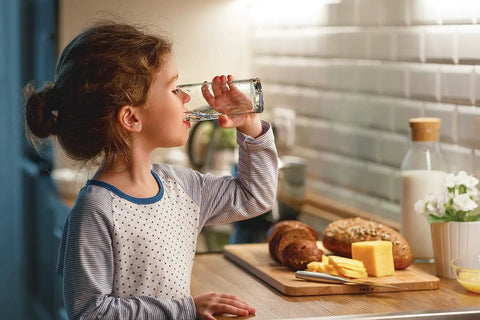 Child drinking water from glass by kitchen counter with bread and cheese, highlighting safe water from Water and Air Filter Combo Pack 2 Piece Set for Select Models WF3CB PAULTRA Reduces Chlorine Taste and Odor Lead Mercury Pharmaceuticals and More Keeps Water Taste Fresh and Fridge Odors In Check.