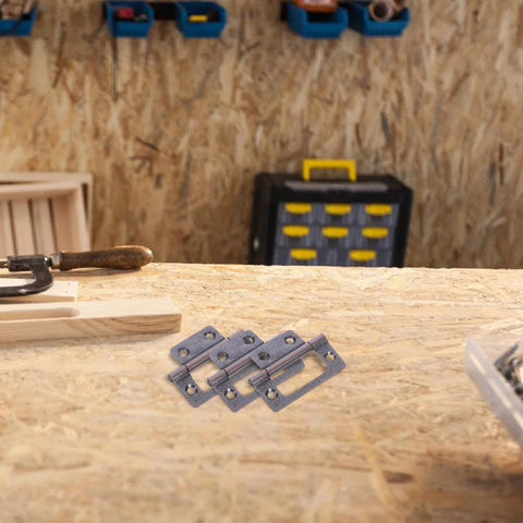 Front view: ten stainless steel cabinet hinge plates with screw holes on a wooden workbench