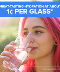 Close-up of a woman with bright pink hair drinking water from a clear glass outdoors.