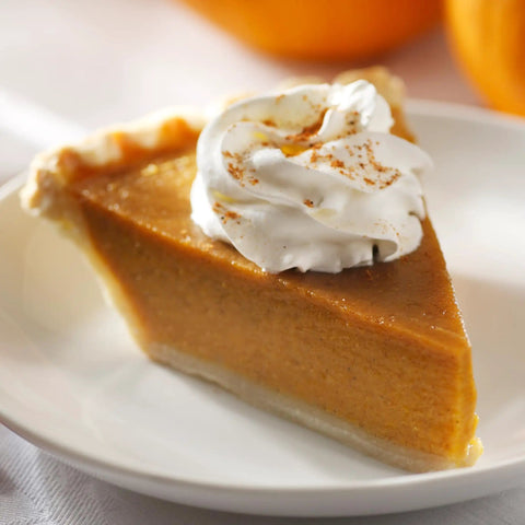 Slice of pumpkin pie with whipped cream on a white plate, focus on the creamy texture and sprinkled spices.