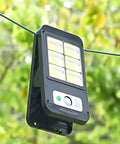 Wall-mounted solar light with motion sensor, black with LED panel, outdoor use against green foliage background
