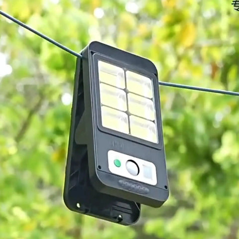 Wall-mounted solar light with motion sensor, black with LED panel, outdoor use against green foliage background