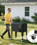 Man pushing black 60 Quart Rolling Patio Cooler Cart With Bottle Opener Cap Catcher And Drain Large Beverage Trolley for Patio Parties Beach Bbq Poolside. Features include handle and 4 wheels.
