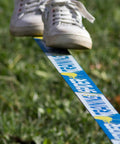 Close-up of sneakers balancing on Ultimate 60 Ft Slackline Training Kit For Beginners With Ratchet stretched over grass