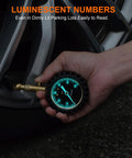 Tire pressure gauge with a 2-inch glowing blue dial, shown in a close-up near a car tire valve.