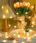 Warm White LED Star String Lights 10 Ft Battery Operated For Indoor Outdoor Decor, draped over table with flowers and lamp